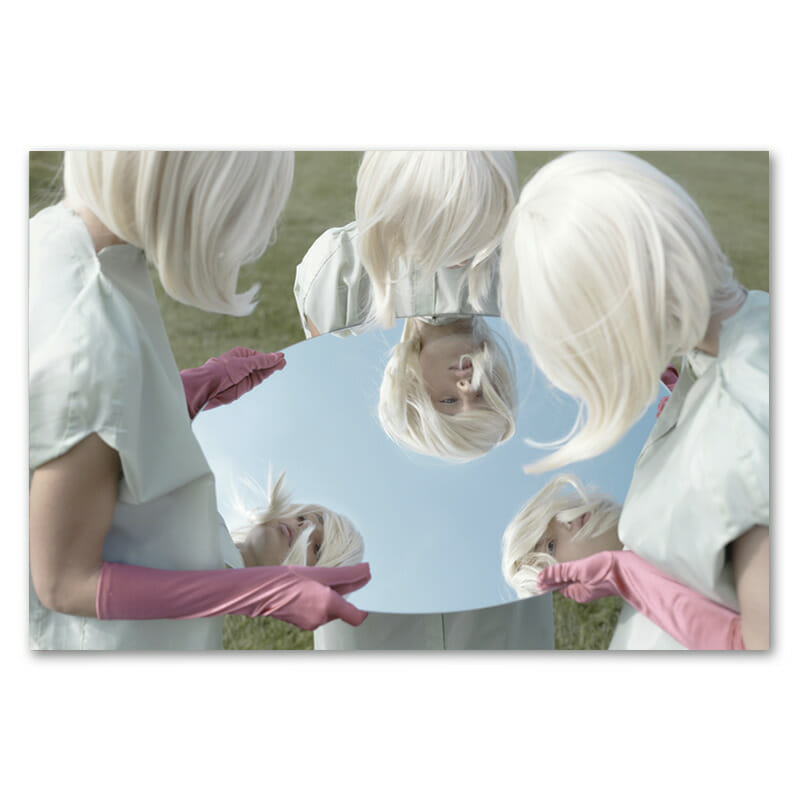 three blonde women wearing pink gloves holding a round mirror looking at themselves