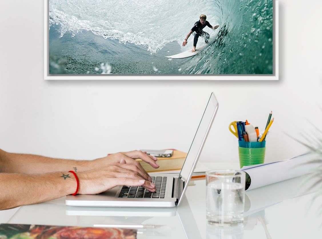 man typing on laptop with photo of surfur on wave
