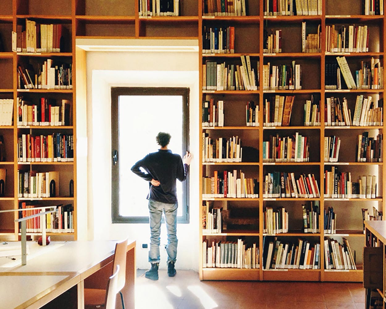 man in library standing looking out the window